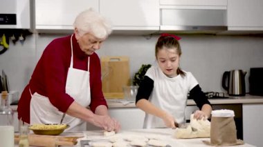 Büyükanne ve torun evde masada turta hazırlıyorlar. Çocuk, ninenin gözetiminde bıçakla hamuru cesurca kesiyor. Güzel küçük kız, mantar hamuruyla iyi iş çıkarıyor.