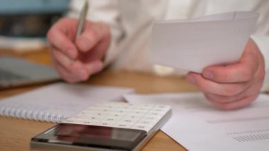 Aylık ev giderlerini hesaplayan adam, vergiler, banka hesabı bakiyesi ve kredi kartı faturaları. Modern bilgisayar kullanan profesyonel bir erkek ofis masasında oturuyor.