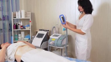Güzellik uzmanı, güzellik kliniğinde kadın hasta vücuduna sensör uyguluyor. Tıbbi yağ temizleme cihazı. Yağ, aşırı kilolu ve selülit sorunu tedavisi