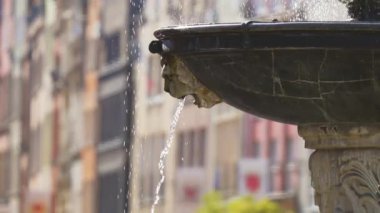 Yoğun Şehir Meydanı 'ndaki dekoratif Çeşmeden Gün Işığı Altındaki Renkli Binalarla Dolu Su Nazikçe Akıyor. Dekoratif fıskiyeler, dalgalı binalarla çevrili, çağlayan suları içerir.