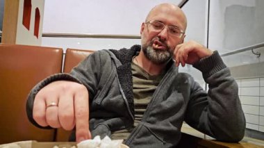 Genç sakallı adam lezzetli patates kızartması yiyor ve fast food restoranının tadını yakından beğeniyor. Zararlı ve sağlıksız yiyecekler. Aç adam kafede ya da restoranda patates kızartması yiyor. Kapat.