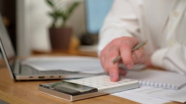 Hesap makinesi uygulaması kullanan erkek eli hesaplama masraflarını kapatır. İşadamı çalışma masasında çalışıyor. İş, ev giderleri, bütçe yönetimi, muhasebecilik. Modern teknoloji, internet ve