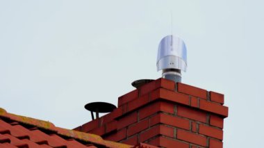 Modern Chimney Cap, Atop Brick Chimney 'i çatıya yerleştirdi, havalandırma ve koruma sağlıyor. Döner türbin, türbülans, baca rüzgar gülü. İyi korunmuş tuğla baca parlak özelliklere sahiptir.
