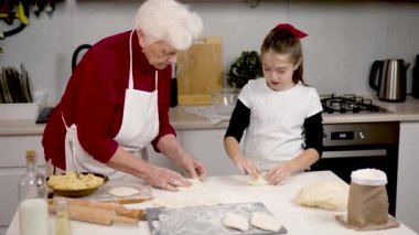 Büyükanne ve torun evde masada turta hazırlıyorlar. Granny 'nin aşçılık dersleri olumlu gidiyor. Güzel küçük kız, mantar hamurunu sıcacık beyaz doldurarak iyi iş çıkarıyor.