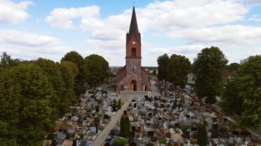 Tarihi Katolik Kilisesi, Tombstone ve Ağaçlarla çevrili Polonya Köyü 'ndeki Mezarlığın Merkezinde Görkemli bir şekilde Duruyor. Polonya 'daki mezarlığın ortasında Katolik katedrali görkemli bir şekilde yükseliyor.