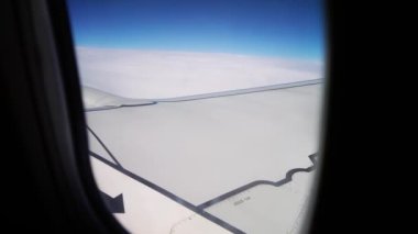 Kanat ve Genişletici Mavi Gökyüzünü gösteren uçak penceresinden, Gündüz Seyahati sırasında Bulutların Üzerindeki Yolculuk. Uçak penceresinden sakin bir manzara, pürüzsüz bir kanadı yakalıyor ve yumuşak mavi gökyüzünü kesiyor.