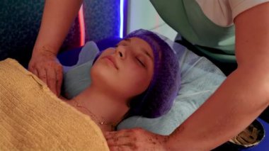 Kadın masör, güzel genç kadın vücuduna temizleyici krem sürüyor. Ağır çekimde yakın çekim. Güzellik salonunda masaj yaptıran genç bir kadın.