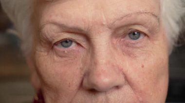 Üst yüz yakın çekim üzgün yaşlı olgun kadın yorgun gri gözler, siyah rimel kameraya bakıyor. Makyajlı son sınıf öğrencisi, cildinde kırışıklıklar var.