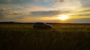 SUV kırsal tarım alanlarında geziniyor. Gün batımı güçlü 4x4 arabasıyla yola çıktı. Kırsal yollarda yaz tatili yolculuğu