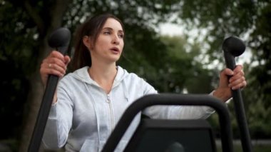 Terli kız dışarıda sıkı bir eğitimden sonra dinleniyor. Kadın derin nefes alıyor. Eliptik formda kilo vermek için yoğun bir egzersiz. Kadın, spor aletlerini kullanarak, dış mekandaki spor rutinini seviyor.