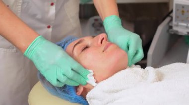 Yakından, kozmetik uzmanı, tıbbi eldivenlerle, özel ıslak mendilli kadın yüzünden kozmetik yüz maskesi kalıntılarını çıkarır. Yüz derisi ve yaşlanma karşıtı. Güzellik tedavi konsepti