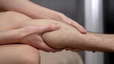 Adam bacak kaslarına kendi kendine masaj yapıyor. Genç adam bacak kaslarına masaj yapıyor. Genç çocuk kendine bacak kası masajı yapıyor.