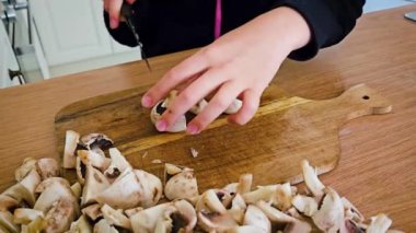 İyi-Aydınlatılmış Mutfak Gündüz Hazırlığı sırasında Ahşap Tahta Masa Mantarları Ustaca Kesiyor. Tanınmayan kız, şampiyon mantarlarını büyük bir bıçakla kesiyor. Dişi ergen anne yemeklerine yardım ediyor.