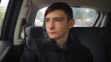 Ergen çocuk bulutlu bir günde düşünceli bir şekilde arabanın arka koltuğundan şehre doğru yol alıyor. 14 yaşında bir çocuk. Araç içinde. Araba gezisinde.