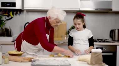 Becerikli yaşlı kadın öğretmen küçük kız ana sınıfı ev yapımı turtalar ve moda mutfakta dolma konusunda ders veriyor. Hamur üzerinde patates. Büyükannem torununa hamur pişirmeyi öğretiyor.