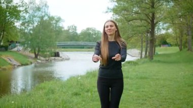 Nehirde dans eden neşeli genç bir kadın basit hareketler yapıyor. Neşeli dişi suyun yanında zarifçe hareket ediyor ve temel adımları atıyor. Nehir kıyısında sallanan mutlu bayan kolay hareketler gösteriyor.