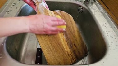Konforlu ev ortamında mutfak işleri sırasında lavabo ve suyla ahşap kesme tahtasını temizlemek. Tanınmayan ev kadını elleriyle lavaboda ahşap kesme tahtasını yıkıyor. Sorumluluk.