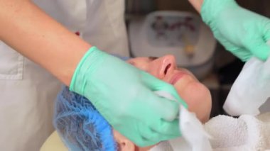 Güzellik uzmanları kozmetoloji ameliyatından sonra kadının yüzünü peçeteyle siliyorlar. Kozmetik prosedürü. Spa tedavisi konsepti. Yüz tedavisi