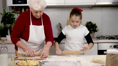 Büyükanne ve torun, mutfakta ahşap oklamalı hamurdan parçalar yapıyorlar. Büyükanne küçük kıza patatesli turta pişirmeyi öğretiyor. Ev işi ekip çalışması yardım ediyor