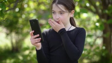 Açık havada cep telefonu kullanan genç bir kızın duygusal video konuşması. Park 'ta akıllı telefondan konuşan genç bir kızın samimi görüntülü sohbeti. Etkileyici genç bir kızın video diyalogları