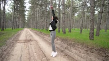 Genç oyuncu kadın zıplıyor, kollarını sallıyor ve doğada eğleniyor. Genç bayan hoplayıp zıplıyor, ellerini sallıyor ve dışarıda eğleniyor. Güzel genç bayan el sallıyor ve kutluyor.