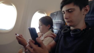 Uçuş sırasında cep telefonlarını kullanarak tek başına uçakla seyahat eden çocuklar. Oğlan ve kız uçakta birlikte oturur, cep telefonlarına odaklanır, yetişkinler olmadan seyahat ederler.
