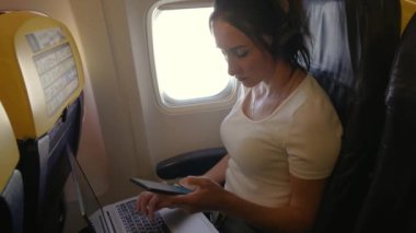 Uçaktaki koltuğundan başka bir ülkeye iş gezisine giderken dizüstü bilgisayarında çalışan bir kadın. Sıradan giysili bir kadın uçakta otururken dizüstü bilgisayarına odaklanır.