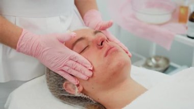 Cilt kozmetoloji salonu nazik tekniklerle profesyonel bakım sunuyor. Yetenekli kozmetik uzmanının rahatlatıcı yüz masajı sırasında uzanan kadın. Tedavinin keyfini çıkaran kadın gençleşmeye odaklandı