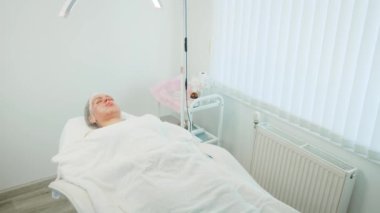 Müşteri estetik ameliyat sonrası anestezi altında yatıyor. Hasta klinik ekipmanlarla tedavi masasında dinleniyor. Parlak tıbbi ortamda ameliyat sonrası iyileşme süreci