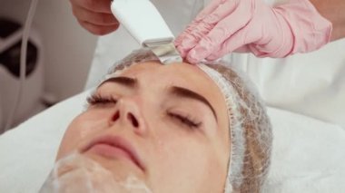 Estetik merkezde cilt bakımı sırasında ultrasonik yüz cihazı kullanan bir profesyonel. İstilacı olmayan teknoloji derin temizlik ve gençleştirme için uygulandı. Alıcı alırken dinleniyor