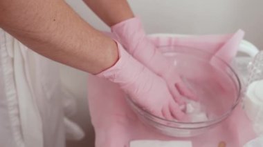 Elleri pembe eldivenli, aletleri suyla dolu kasede hazırlayan eller. Hijyenik güzellik prosedürü için malzemelere dikkat edin. Temizliği ve tedaviye hazır olmayı güvence altına alan kusursuz bir hazırlık
