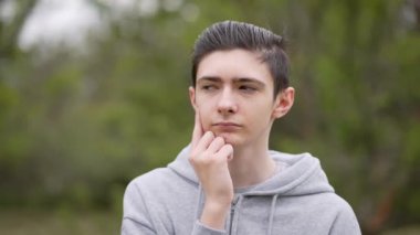 Ergen düşünceli bir şekilde açık havada bir şeyler düşünüyor. Doğanın derinliklerinde yatan genç bir çocuk. Ergenlik çağındaki erkek temiz havayı dikkatlice düşünüyor.