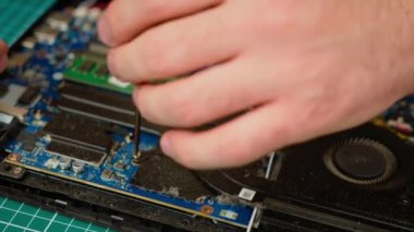 Eller dizüstü bilgisayar bileşenlerini tamir ediyor, tornavida tutuyor ve iç parçalar üzerinde dikkatlice çalışıyor. Avuçlar ana kartı onarıyor, donanımı hassasiyetle ayarlıyor. Parmaklar devre kartını incelikle ayarlıyor.