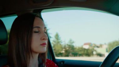 Odaklanmış ifadesi olan bir kadın araba kullanıyor, elleri kendine güvenen bir şekilde direksiyonu tutuyor. Yolda giderken azim ve sakinlik gösteren kadın sürücü