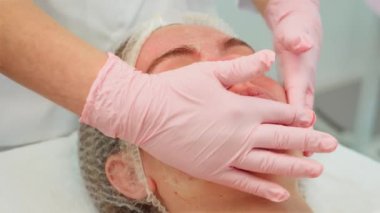 Yumuşak bir uygulama için eldivenli eldiven ile yapılan kadın yüz masajı. Dişi, nazik tekniklerle cilt bakımını gevşetiyor. Dağıtıma odaklanan uzmanlar ve