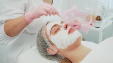 Kozmetik bilimci tarafından ahşap aplikatör kullanılarak pembe eldivenli yaşlanma önleyici maske takılıyor. Cilt bakımı, hastamız kapalı gözlerle rahatça yatarken yapılır. Profesyonel güzellik uzmanıyım.