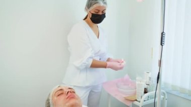 Kozmetik uzmanı tarafından cilt bakımı için hazırlanmış ıslak yüz bezleri. Yüz maskesi takılmış bir kadın tedavi yatağında dinleniyor. Profesyonel bakım ve bir sonraki adımlar için hazırlık.