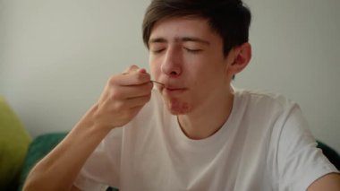 Çocuk pasta yiyor. Beyaz tişörtlü bir erkek kaşık tutuyor. Genç adam tatlıyı içeride yiyor.