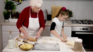 Un ve hamur hamurunu tortilla şeklinde yuvarlayan tatlı bir kıza yemek pişirmeyi öğreten mutlu bir büyükanne. Doldurulmuş çörekler. Büyükanne ve torun. Mutfakta eğlence için pişirmek, öğrenmek.