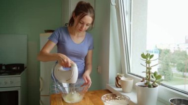 Kadın cam kasede yumurta beyazı çırpıyor elektrikli karıştırıcı kullanıyor, kabarık hamuru hazırlıyor. Pişirme işlemi sırasında kadın karışımı ile el bilgisayarı karıştırıcı karışımı. Bayan mutfakta havadar bir doku yaratıyor.