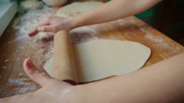 Kızınız un kaplı yüzeyinde ahşap oklamalı hamuru yuvarlıyor. Yemek hazırlıkları sırasında hamuru düzleştiren kız. Gelecek tarif için hamuru eşit şekilde şekillendirmek için merdane kullanan çocuk