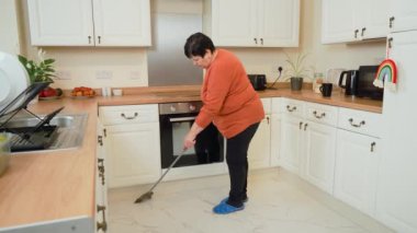 Kadın süpürgeyle mutfak zeminini süpürüyor. Kadın temizliği mutfakta fayanslarla yapılmış. Modern iç dekorasyonda yerleri düzenleyen kadın.