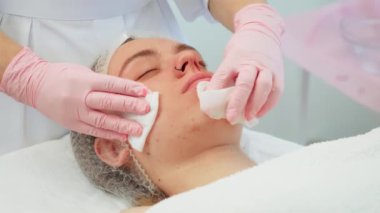 Eldivenli ellerle pamuk pedlerle yüzünü temizlerken kadın rahat uzanıyor. Cilt bakımı sırasında yüz temizleme ameliyatı olan bir kadın. Uzmanlardan nazik cilt bakımı gören bir bayan.