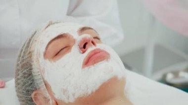Yenileyici yüz maskesi cildini kapatıyordu. Gözleri sakince kapalıydı. Cilt bakımını ve su kaybını iyileştirmek amacıyla cilt bakımını seven genç bir bayan. Kız alıyor