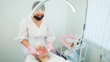 Profesyonel güzellik uzmanı yenilenme prosedürü. Parlak lamba altında yüz temizleme ile. Cilt bakımı sırasında uzanan kadın cilt sağlığını iyileştirmeye odaklanmış. Kozmetik uzmanı