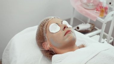 Müşteri dermatoloji ofisinde yüz tedavisini canlandırıyor. Hidratlaştırıcı maskeli bir kadın, cilt sağlığını arttırıyor. Oturum sırasında hassas bölgeleri sakinleştirmek için pamuk pedleri