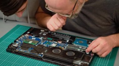 Baba oğul dizüstü bilgisayar bileşenlerini inceliyor, onarım seçeneklerini değerlendiriyor. Erkek ve çocuk defter iç kısımlarını yakından inceliyor, düzeltmeleri tartışıyorlar. Bilgisayar parçalarını inceleyen çocuk ve adam beyin fırtınası yapıyor.