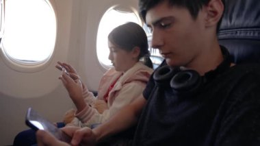 Çağdaş Uçak Ayarları 'nda Yalnız Seyahat Eden Çocuklar Uçuşta Cep Telefonları ile Nişanlı. Oğlan ve kız uçakta tek başlarına seyahat ederken akıllı telefonlara odaklanmışlar.