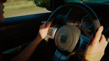 Eller direksiyonda güneşli kırsal yolda araba sürüyor. Sakin bir günde parmaklar direksiyonda geziniyor. Sürücü arabası sıcak bir yolculuğun tadını çıkarıyor.