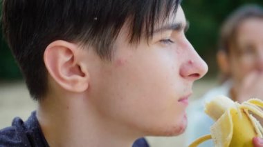 Annesiyle muz yiyen çocuk, odaklanmış ifade gösteriyor. Annesiyle muz yiyen, konsantrasyon gösteren bir erkek. Annesiyle muz yiyen adam, sakin bir tavır sergiliyor.